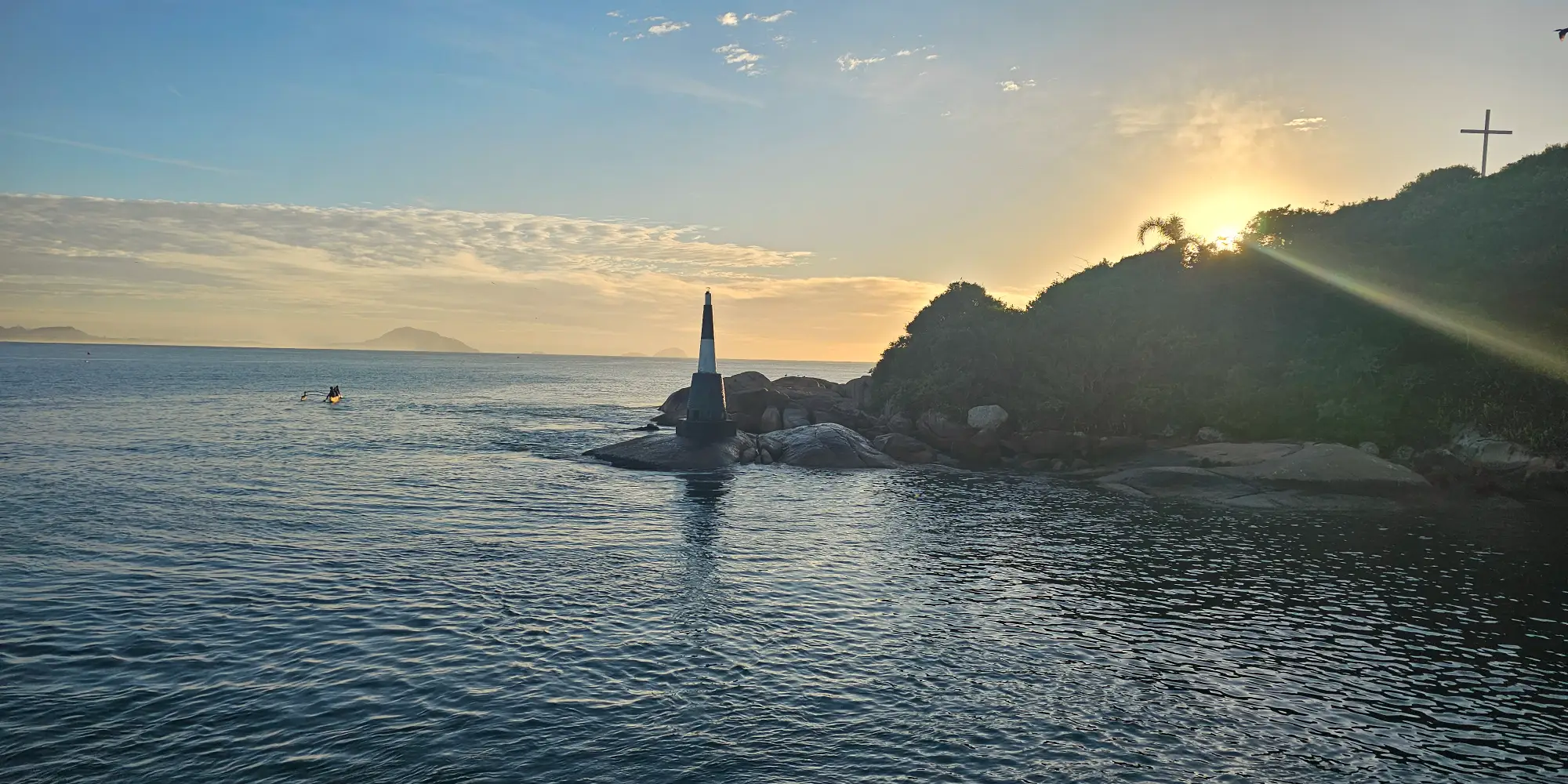 Amanhecer no molhe da Barra da Lagoa, com o farol e uma canoa havaiana ao longe