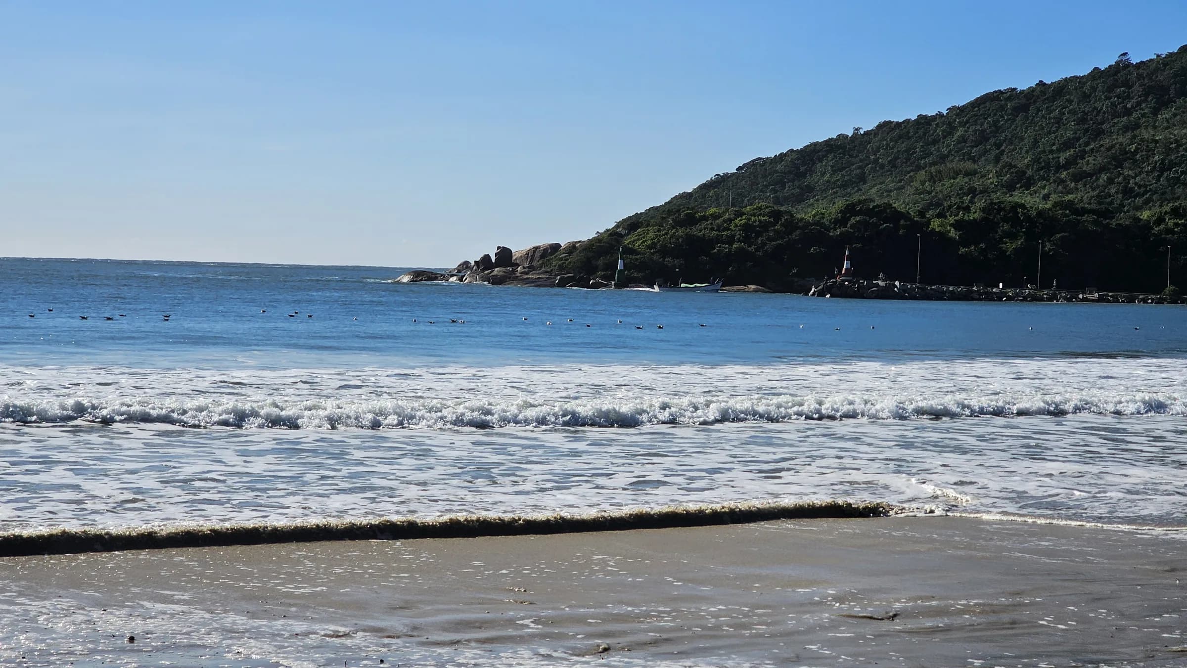 Praia da Barra da Lagoa, em Florianópolis, com o molhe e o morro ao fundo